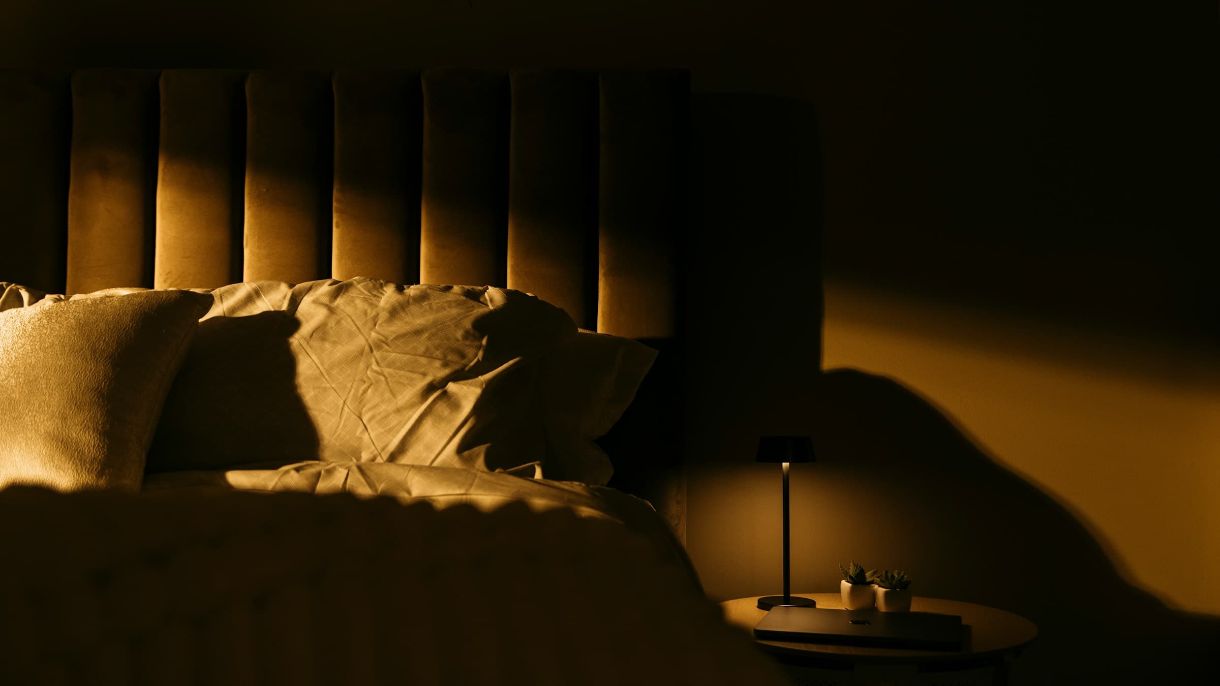 Warm, dimly lit bedroom with soft pillows and a nightstand lamp, creating a calming sleep
environment for a healthy nighttime routine.