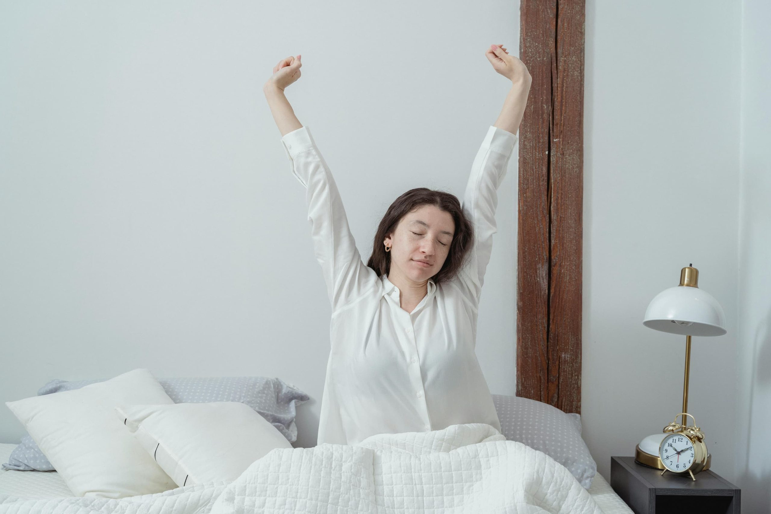 Woman stretching in bed after a restful night’s sleep, promoting the benefits of a consistent sleep schedule and natural sleep support.