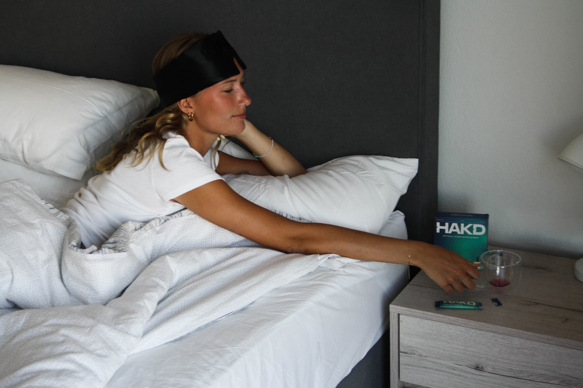 Woman in bed wearing a sleep mask after taking HAKD Health Night Blend, a natural cherry-flavoured sleep supplement for better nighttime recovery.