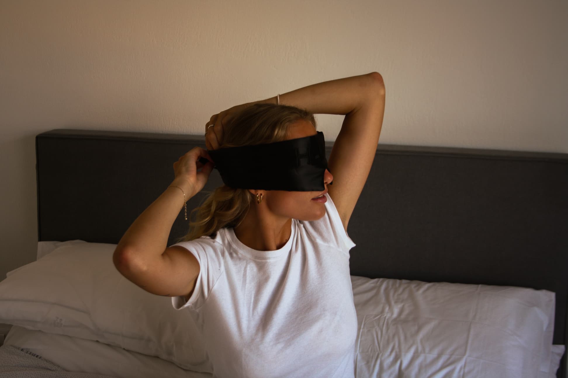 Woman putting on HAKD Health silk blackout eye mask as part of her bedtime routine to block light and improve sleep quality naturally.