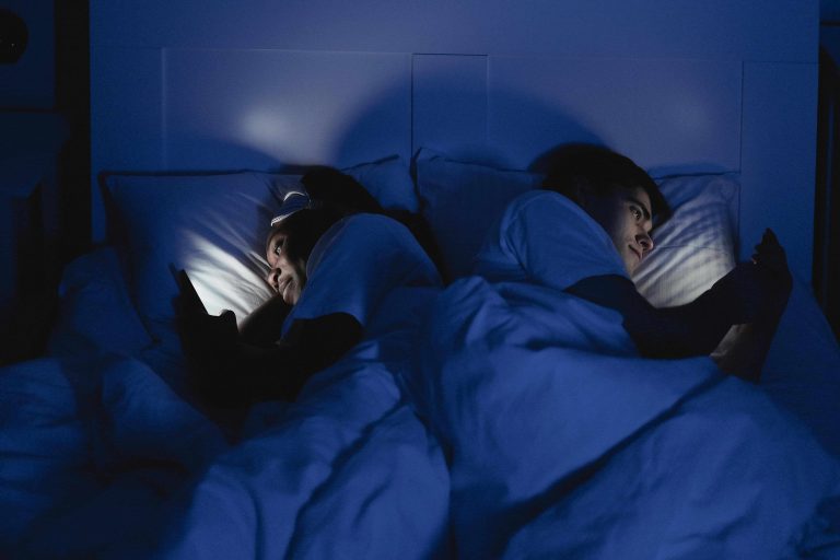 Couple on phones in bed at night, showing how screen time disrupts deep sleep