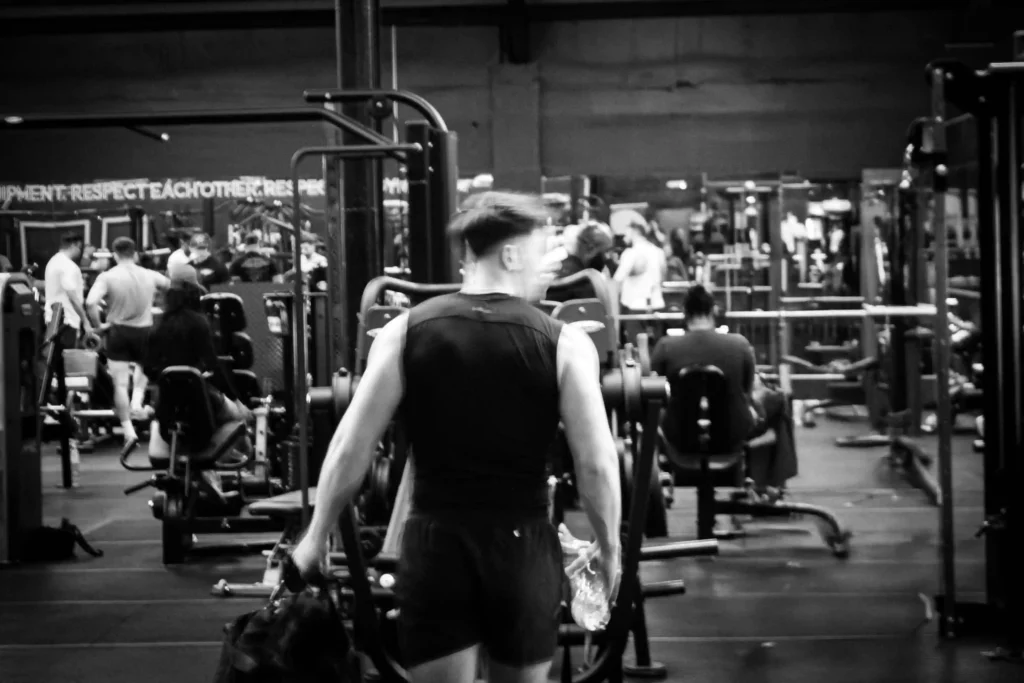 Gymgoer walking through busy gym floor after workout, representing how proper rest from HAKD Night Blend powers next-day performance and recovery