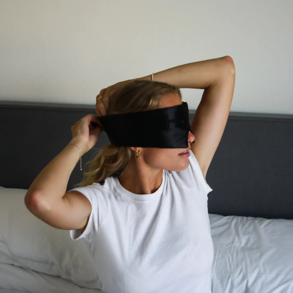 Woman putting on the HAKD Deep Sleep Mask before bed to block light and enhance sleep quality. 