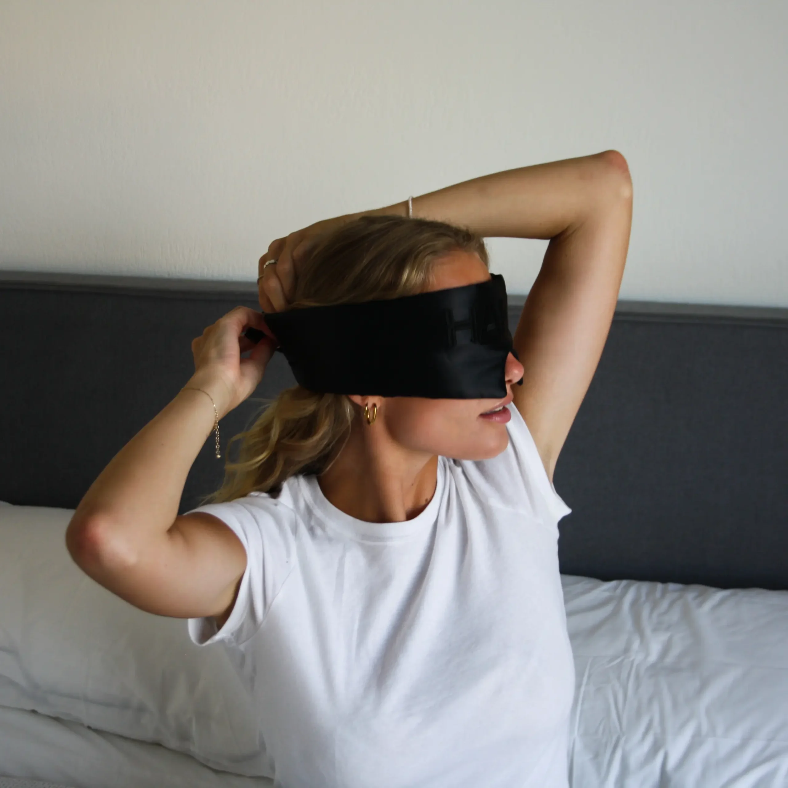 Woman putting on the HAKD Deep Sleep Mask before bed to block light and enhance sleep quality.