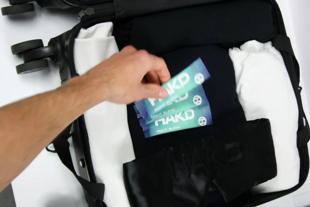 Packing HAKD Night Blend sachets and Deep Sleep Mask into a suitcase - your portable sleep system for travel and recovery.