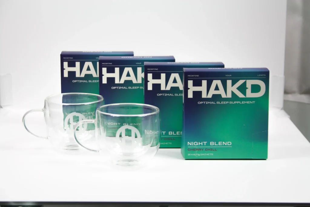 HAKD Night Blend supplement boxes and branded glass mugs displayed, highlighting the Cherry Chill flavour and sleek product design for sleep support