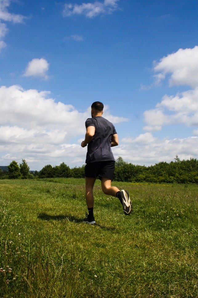 Man running outdoors on a sunny day in an open field, representing fitness, health, and active recovery.