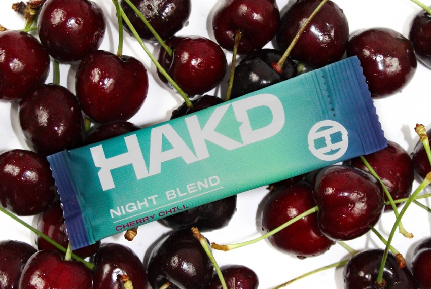 HAKD Night Blend Cherry Chill sleep supplement sachet surrounded by fresh cherries, highlighting its natural cherry flavour.