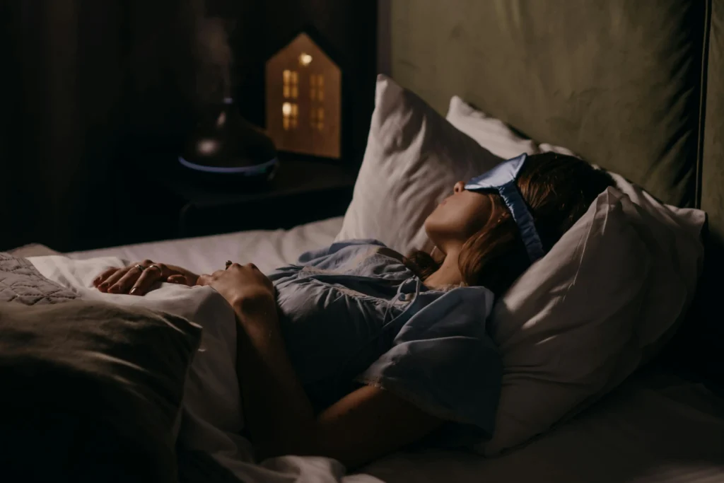 Woman sleeping in a dark bedroom while wearing a sleep mask, creating an optimal environment for deep, restorative rest.