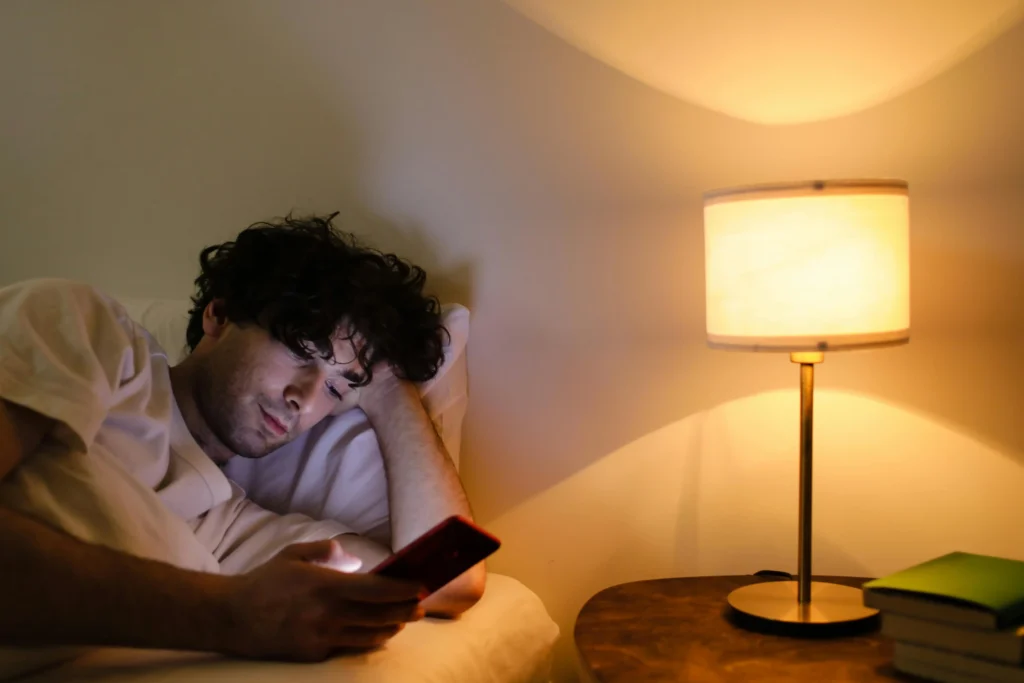 Man using a smartphone in bed at night, exposing himself to blue light that can disrupt sleep