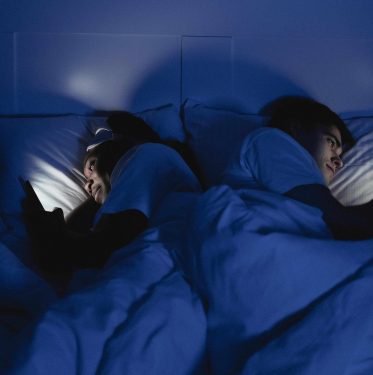 Couple on phones in bed at night, showing how screen time disrupts deep sleep