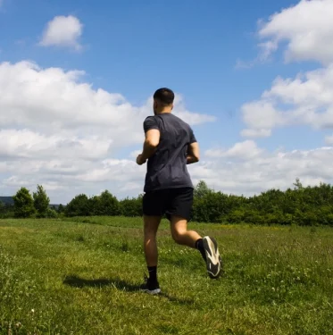 Man running outdoors on a sunny day in an open field, representing fitness, health, and active recovery.