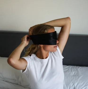 Woman putting on the HAKD Deep Sleep Mask before bed to block light and enhance sleep quality.