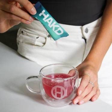 HAKD Night Blend sleep supplement being poured into a mug of water, demonstrating how to use the sachet for better sleep and recovery.